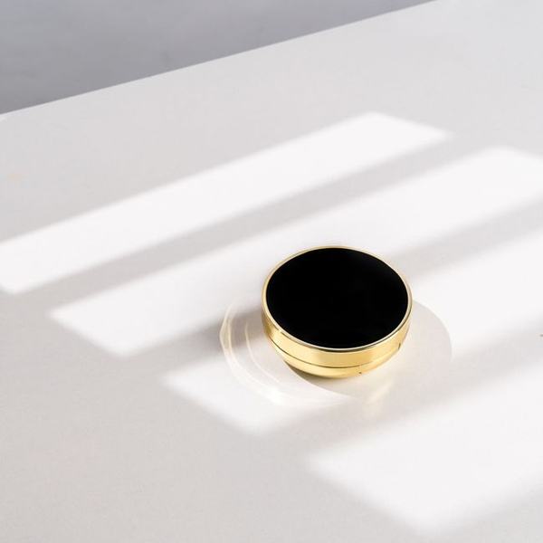 A small black and gold compact case in hard sunlight