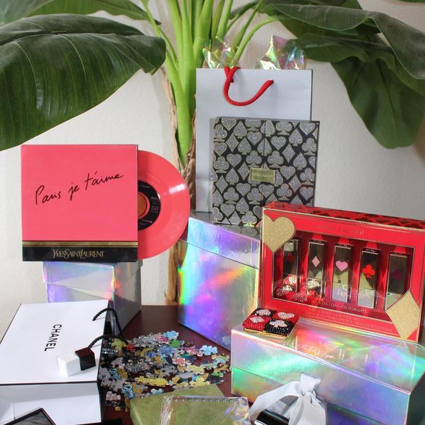 A Yves Saint Laurent pink vinyl record with Estee Lauder, Chanel and Gucci pieces staged around iridescent boxes